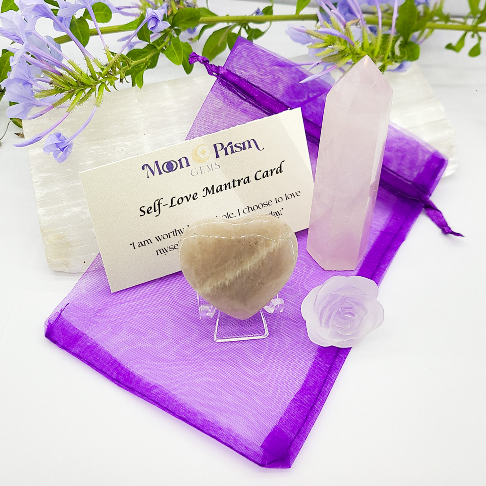Purple crystal, self-love mantra card, and decorative item on a white background with flowers.